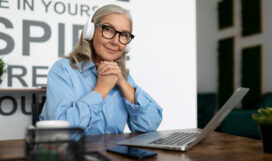 successful mature woman manager watching training video on laptop with headphones sitting at table in office. Accounting Bookkeeper Clerk Woman concept successful woman manager watching training video on laptop with headphones sitting at table in office.